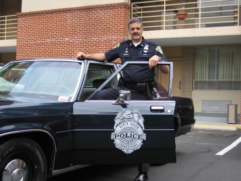1991 Ford LTD Crown Victoria - uniformed officer leans on the open door of a dark police car displaying a North Haven, Connecticut Police badge decal.