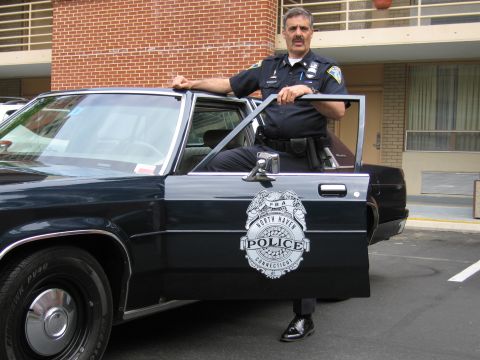1991 Ford LTD Crown Victoria - uniformed officer stands behind the open door of a dark police cruiser bearing a North Haven, Connecticut Police emblem.