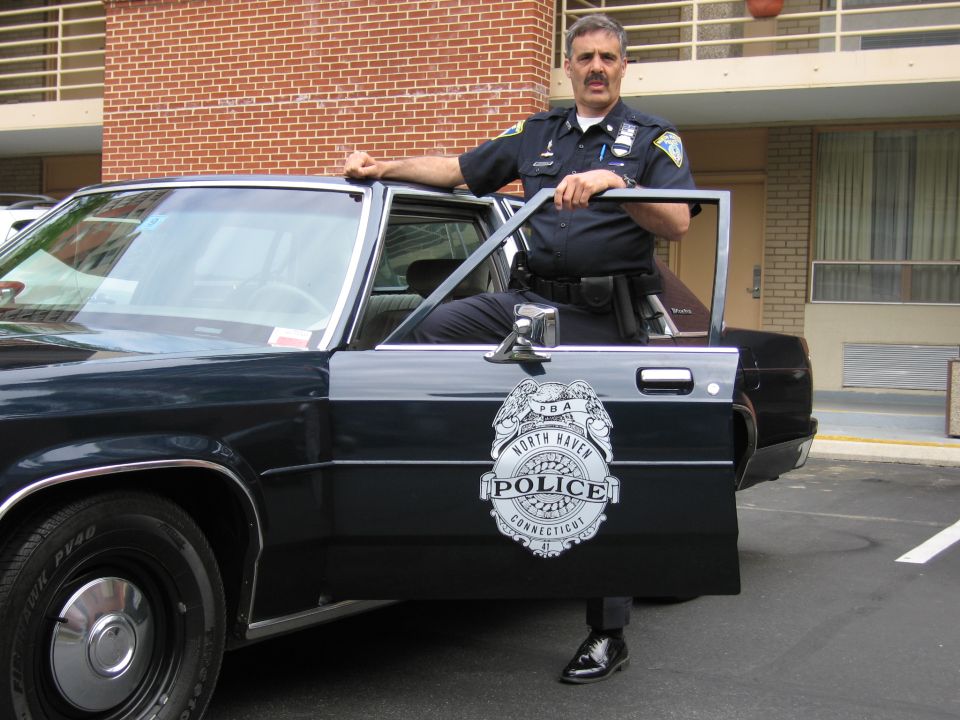 Officer beside open door of dark cruiser showing North Haven Connecticut Police emblem