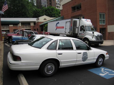 1991 Ford LTD Crown Victoria - White Ford Crown Victoria police cruiser parked in a lot, with an NYPD vehicle and a box truck visible behind it.