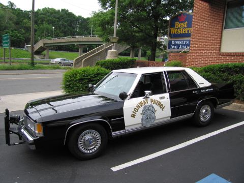 1991 Ford LTD Crown Victoria - black-and-white Ford LTD Crown Victoria Highway Patrol cruiser with push bumper parked outside a Best Western hotel.