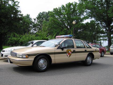 1991 Ford LTD Crown Victoria - tan-and-brown Chevrolet Caprice State Police cruiser with a shield door emblem parked along a tree-lined street.