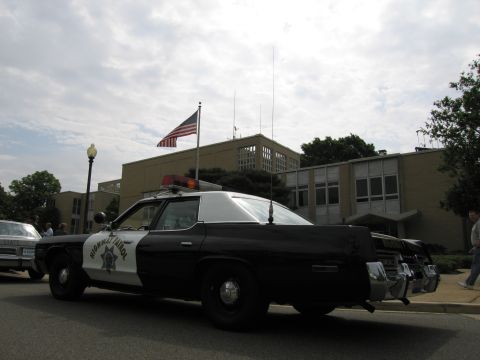 1991 Ford LTD Crown Victoria - Rear three-quarter view of a black-and-white Highway Patrol sedan with roof light bar parked at a curb under a cloudy sky.