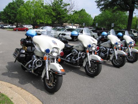 1991 Ford LTD Crown Victoria - Four white police motorcycles, each with a blue helmet on the seat, lined up in a row in a parking lot.