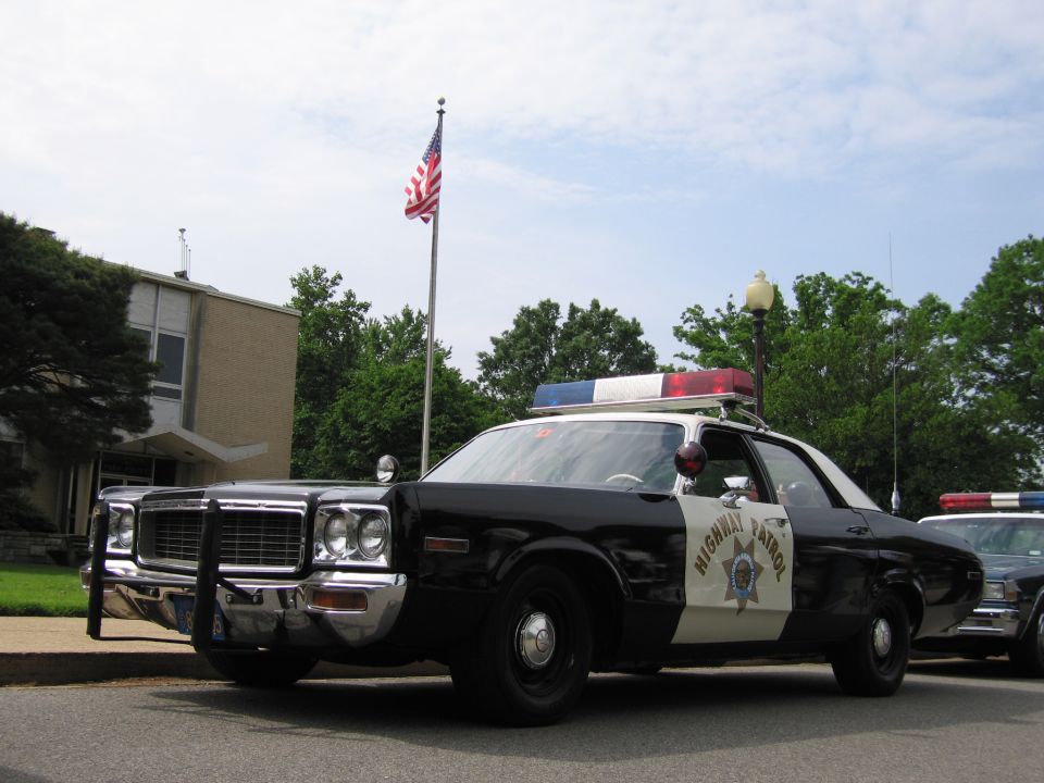 Front of black and white 1970s Highway Patrol sedan with push bumper under U.S. flag