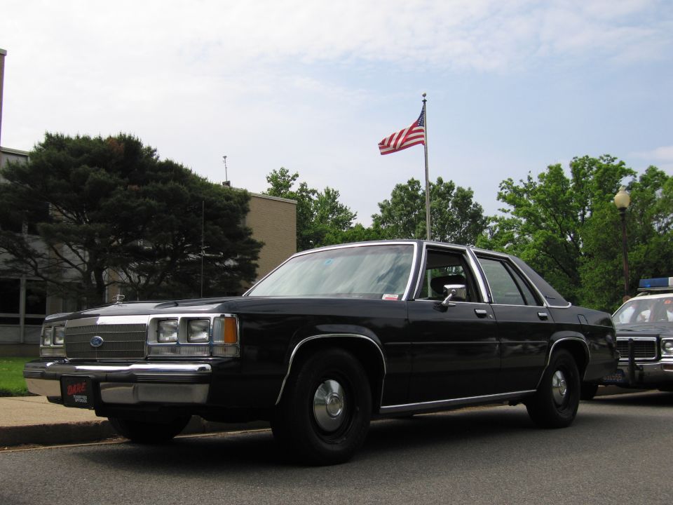 Black Ford LTD Crown Victoria sedan parked at curb beside another police car