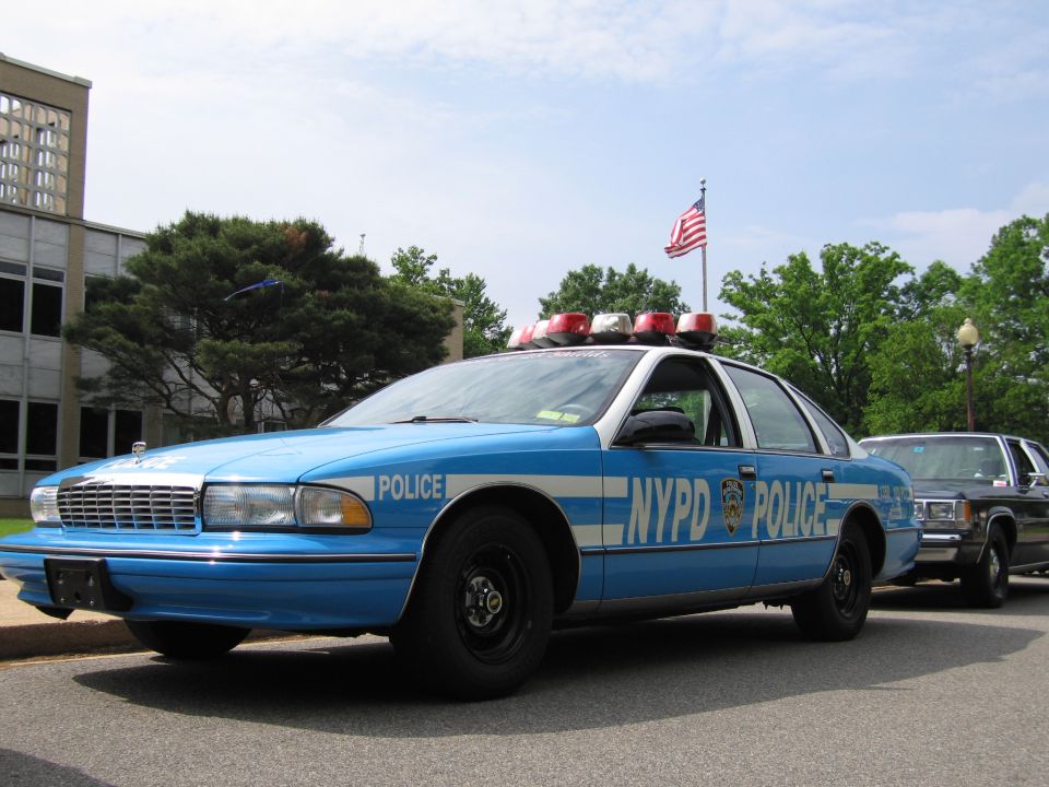 Blue and white NYPD Chevrolet Caprice police car with roof lights parked by building