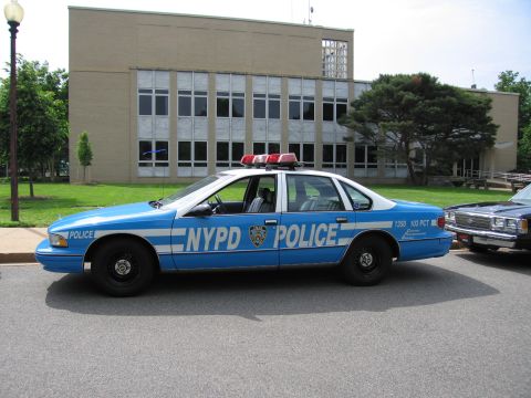 1991 Ford LTD Crown Victoria - blue and white Chevrolet Caprice-style NYPD police cruiser marked POLICE 103 PCT parked along a curb in front of a brick building.
