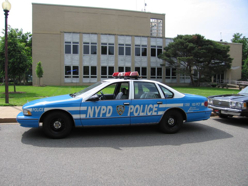 Blue and white NYPD police car parked beside a brick municipal building