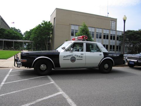 1991 Ford LTD Crown Victoria - black-and-white JAFFREY POLICE sedan with a front push bar and roof light bar parked in a lined lot beside a municipal building.