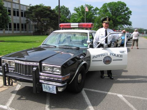 1991 Ford LTD Crown Victoria - uniformed officer in white shirt and cap stands at the open door of a black-and-white JAFFREY POLICE cruiser, plate 169-E.
