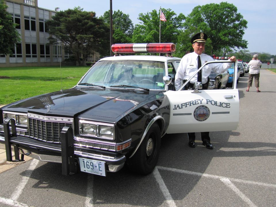 Officer in white uniform standing by open door of Jaffrey Police car