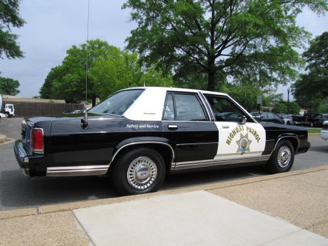 1991 Ford LTD Crown Victoria - Rear three-quarter view of a black-and-white HIGHWAY PATROL sedan lettered Safety and Service with a star door emblem.