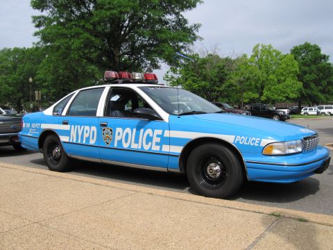 1991 Ford LTD Crown Victoria - blue and white Chevrolet Caprice NYPD POLICE cruiser parked at a curb with trees behind.