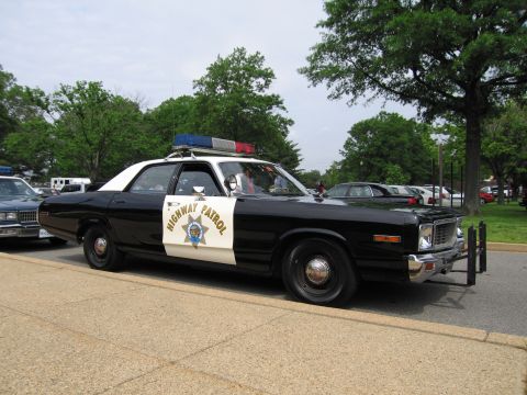 1991 Ford LTD Crown Victoria - black-and-white HIGHWAY PATROL cruiser with a roof light bar and star door emblem parked at a curb under trees.