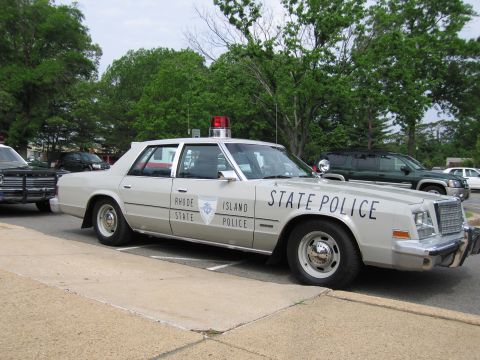 1991 Ford LTD Crown Victoria - cream-colored RHODE ISLAND STATE POLICE four-door sedan with a spotlight, push bar and single roof light parked at a curb.
