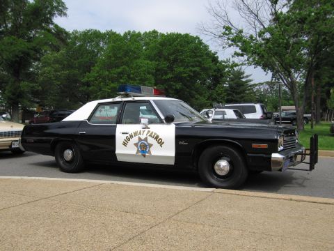 1991 Ford LTD Crown Victoria - black-and-white HIGHWAY PATROL sedan with chrome bumper, push bar and roof light bar parked at a curb among trees.