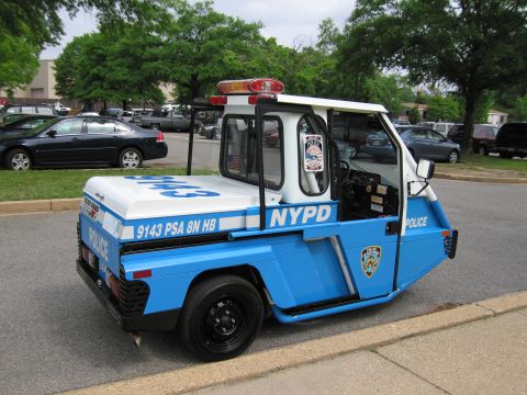 1991 Ford LTD Crown Victoria - blue and white three-wheeled NYPD police scooter cart marked 9143 PSA 8N HB parked at a curb in a lot.