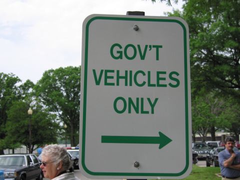 1991 Ford LTD Crown Victoria - Close-up of a green-and-white GOV'T VEHICLES ONLY sign with a right arrow, people and parked cars behind it.