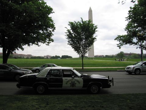 1991 Ford LTD Crown Victoria - black-and-white Highway Patrol cruiser parked on a street with the Washington Monument rising in the background.