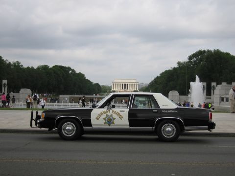 1991 Ford LTD Crown Victoria - Side profile of a black-and-white Highway Patrol cruiser parked before the Lincoln Memorial and a fountain.