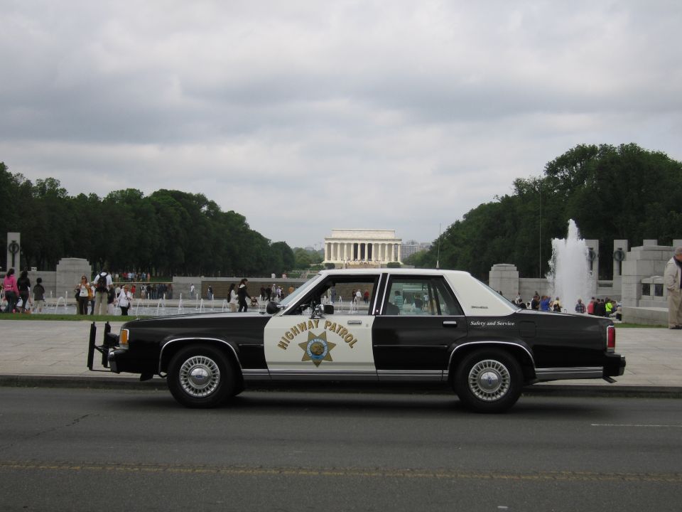 Side view of a black-and-white Highway Patrol sedan parked before the Lincoln Memorial and fountains