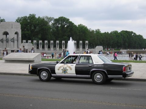 1991 Ford LTD Crown Victoria - black-and-white Highway Patrol Ford cruiser parked beside the World War II Memorial pillars and fountain.