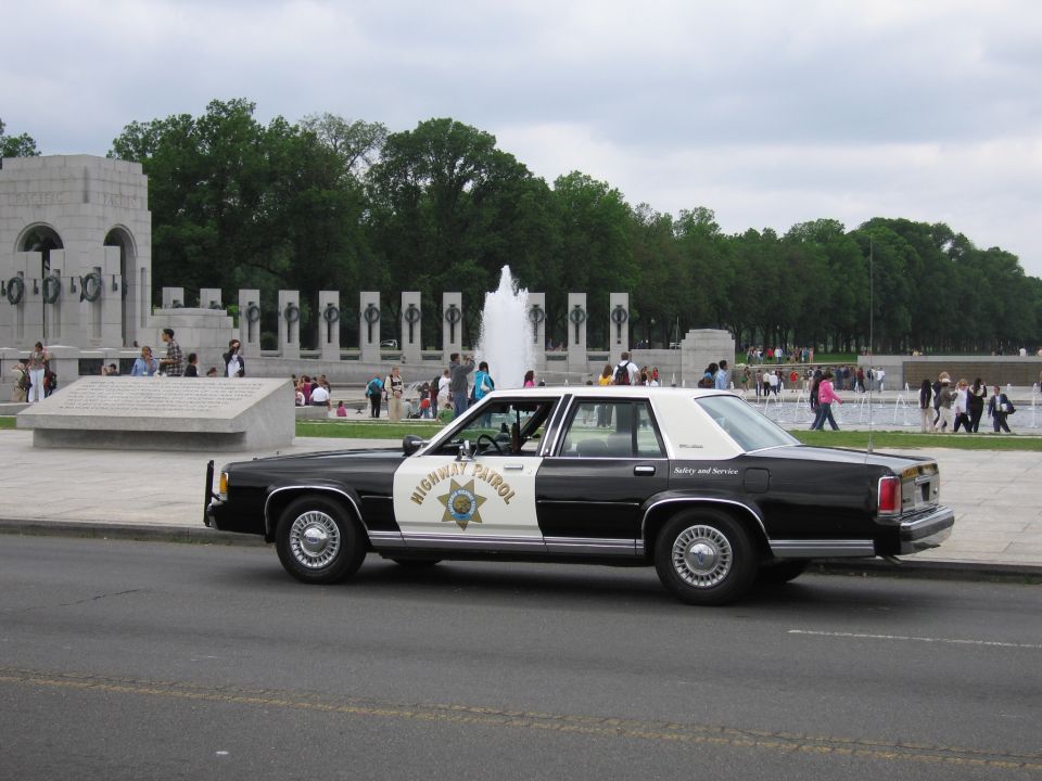 Black-and-white Highway Patrol Ford sedan parked beside the World War II Memorial fountain