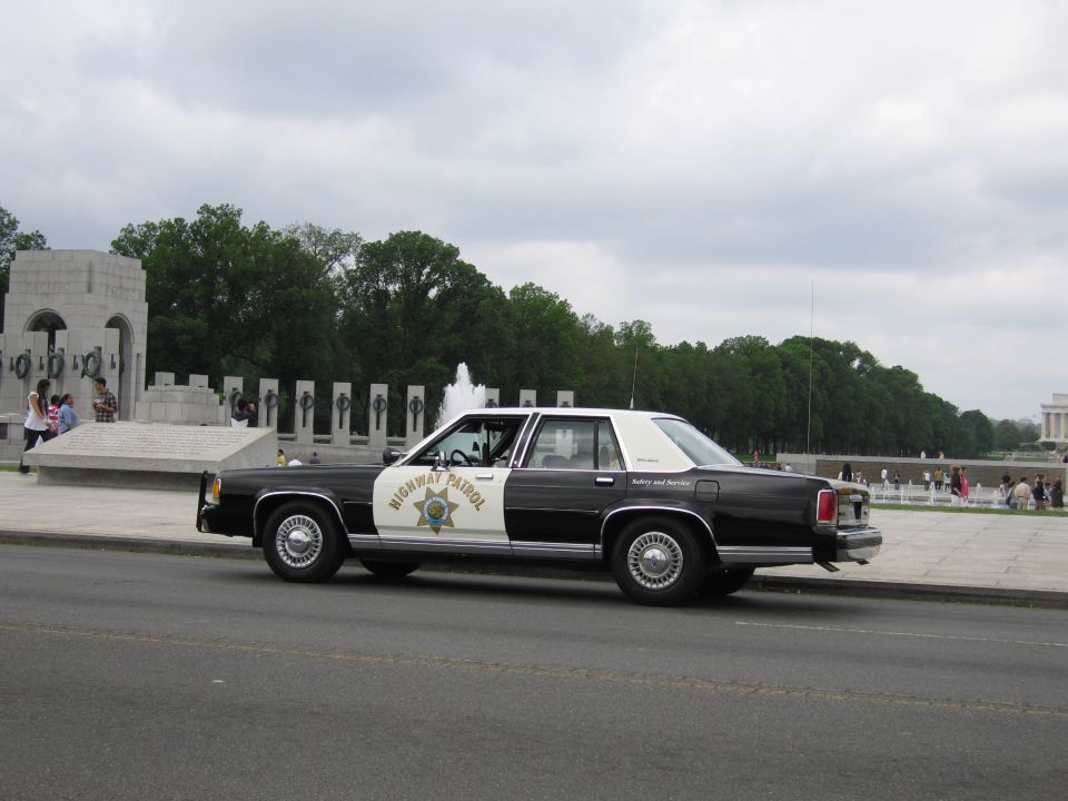 Side view of a black-and-white Highway Patrol sedan at the World War II Memorial with Lincoln Memorial behind