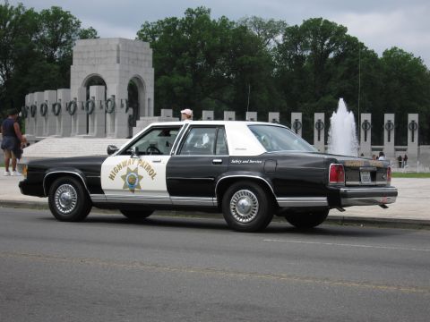 1991 Ford LTD Crown Victoria - black-and-white Highway Patrol cruiser parked at the World War II Memorial with a person standing by the driver door.