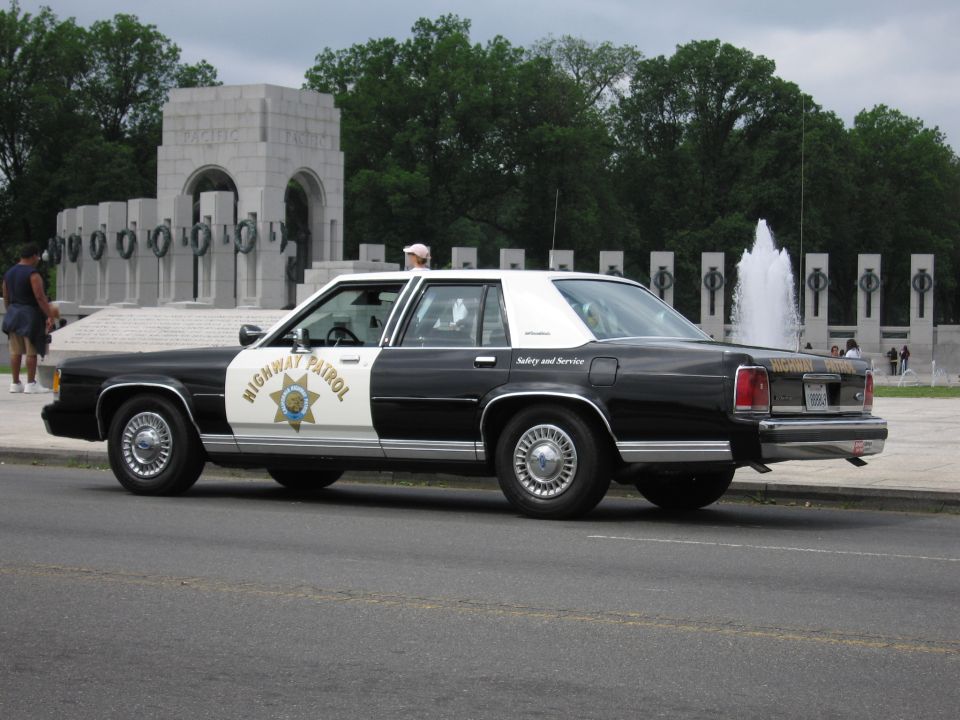 Black-and-white Highway Patrol sedan with a person standing beside it at the World War II Memorial
