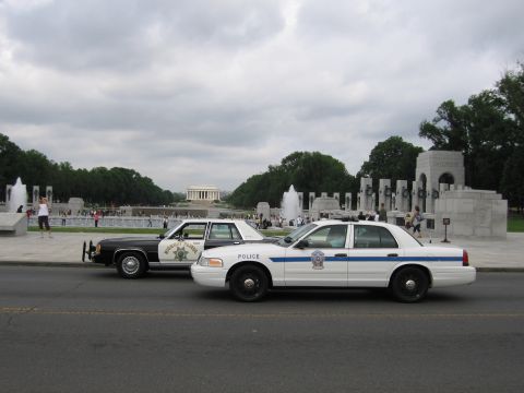 1991 Ford LTD Crown Victoria - white Ford Crown Victoria police car and a black-and-white cruiser parked near the Lincoln Memorial and fountains.