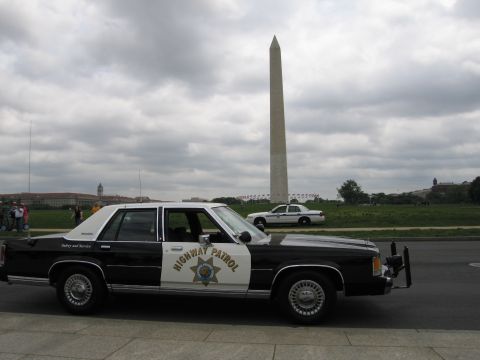 1991 Ford LTD Crown Victoria - Side profile of a black-and-white Highway Patrol cruiser with the Washington Monument rising behind it.