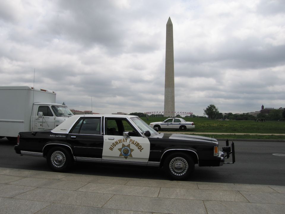 Black-and-white Highway Patrol sedan and a white cruiser parked before the Washington Monument near a truck