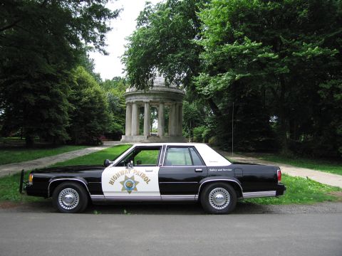 1991 Ford LTD Crown Victoria - black-and-white Highway Patrol cruiser parked on a path before a domed columned stone gazebo in a green park.
