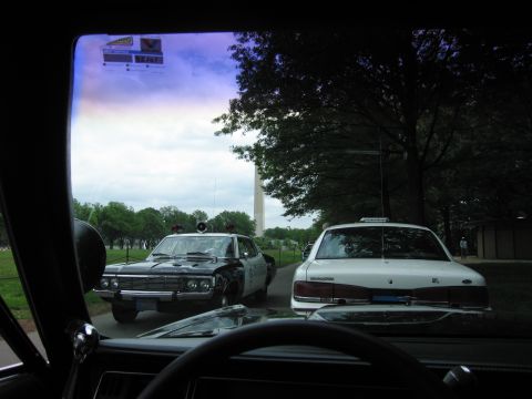 1991 Ford LTD Crown Victoria - Through a windshield, a black-and-white police cruiser and a white patrol car are parked on a path near the Washington Monument.