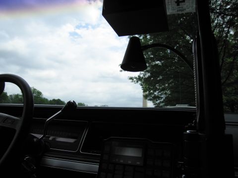 1991 Ford LTD Crown Victoria - Silhouetted car interior showing a steering wheel, dashboard two-way radio, and a gooseneck spotlight against an overcast sky.