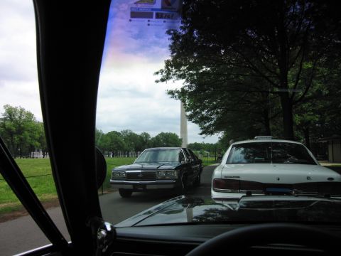 1991 Ford LTD Crown Victoria - Through a windshield, a black-and-white police sedan and a white patrol car are parked on a path before the Washington Monument.