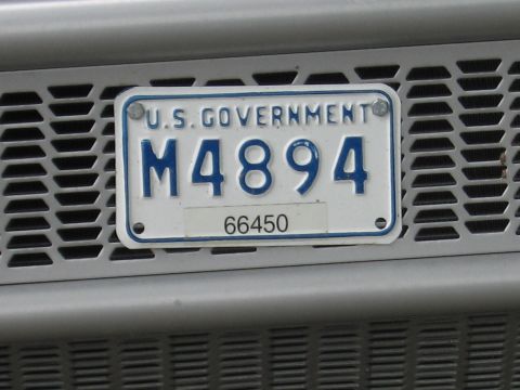 1991 Ford LTD Crown Victoria - Close-up of a white U.S. Government license plate stamped M4894 with a small 66450 tag, mounted on a gray vented grille.
