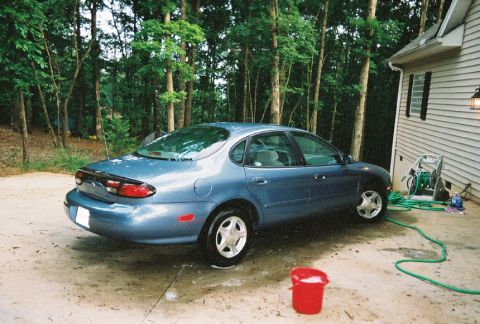 1999 Ford Taurus - A blue 1999 Ford Taurus sedan is parked in a driveway next to a house.