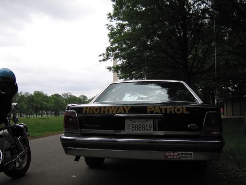 1991 Ford LTD Crown Victoria - Rear view of a black Highway Patrol sedan with gold HIGHWAY PATROL lettering and a California plate, parked near a tall monument.