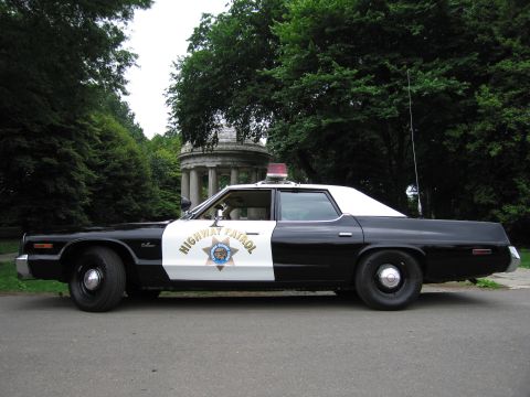 1991 Ford LTD Crown Victoria - Side profile of a 1970s black-and-white Highway Patrol sedan parked on a tree-shaded path in front of a domed monument.