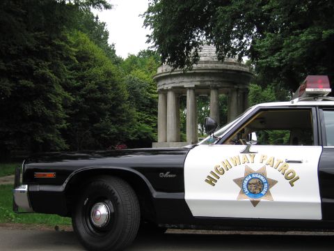 1991 Ford LTD Crown Victoria - Front quarter view of a black-and-white sedan with a California Highway Patrol star door emblem, parked near a domed monument.