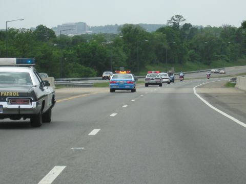 1991 Ford LTD Crown Victoria - Vintage patrol cars with roof lights and motorcycles travel a divided highway lined with trees and overhead lamps.