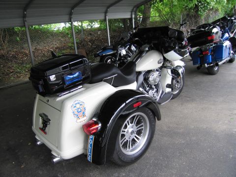 1991 Ford LTD Crown Victoria - white police trike with a winged emblem and POLICE lettering on the rear fender parked beside other motorcycles.
