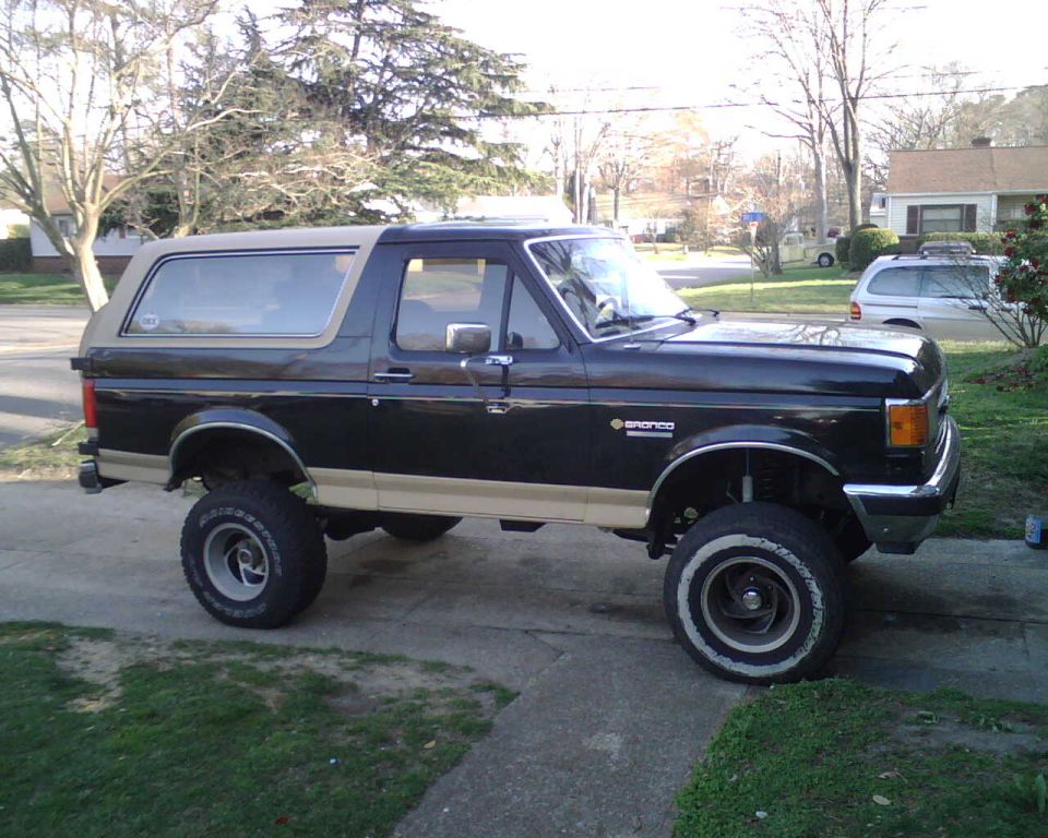Lifted black and tan Ford Bronco on big tires, side view in a residential driveway