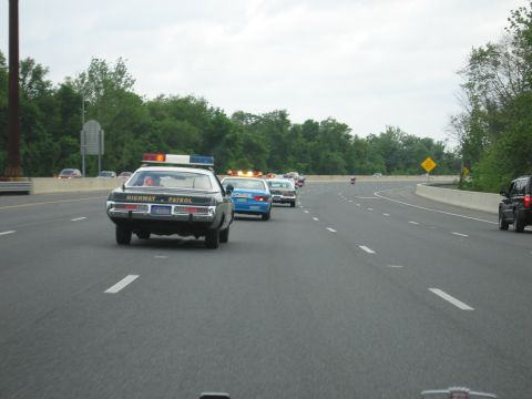 1991 Ford LTD Crown Victoria - Rear view of a Highway Patrol cruiser and a blue Police car with amber lights leading a convoy on the highway.