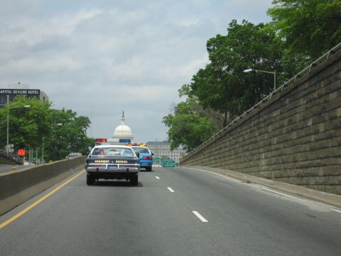 1991 Ford LTD Crown Victoria - black-and-white Highway Patrol car and a blue car head down a sunken roadway toward the U.S. Capitol dome.