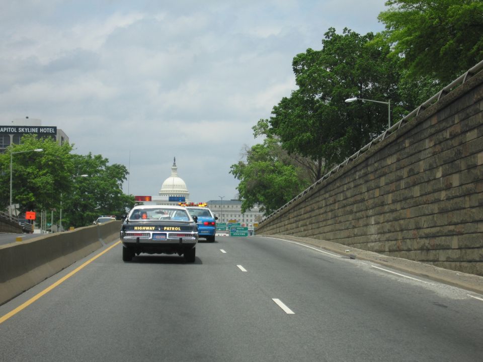 Highway Patrol car and blue car driving toward the U.S. Capitol dome