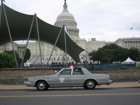 1991 Ford LTD Crown Victoria - silver State Police full-size sedan with rooftop lights sits curbside before the U.S. Capitol and a green canopy.
